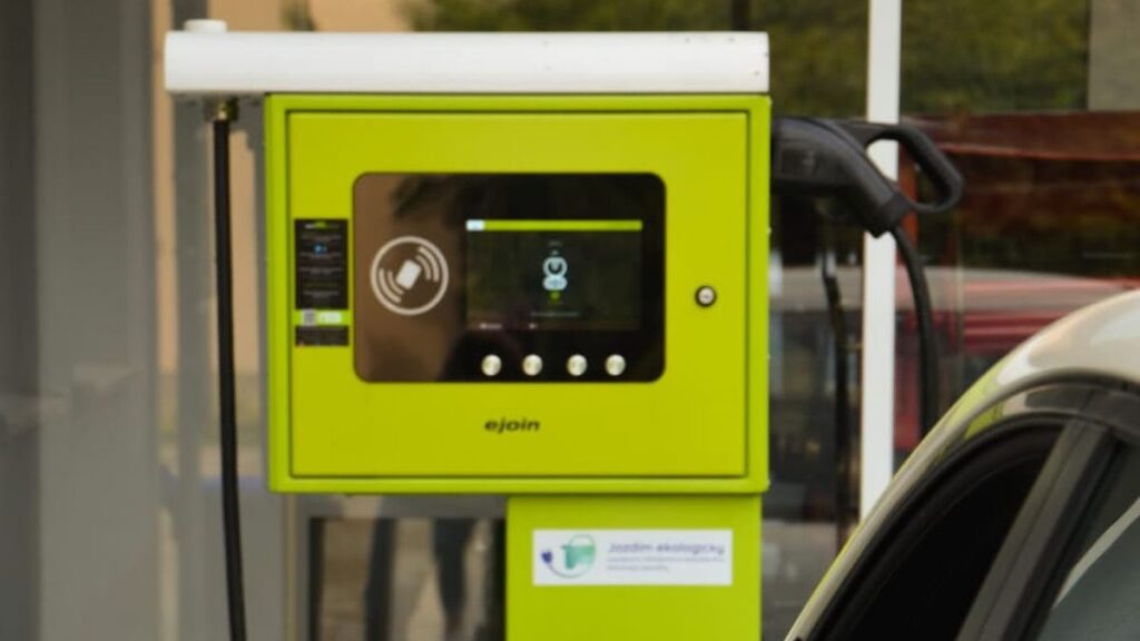 eJoin DC gyorstöltő érintőképernyővel és CCS2 kábellel, mellette elektromos autó – ISO 15118-20 és Plug and Charge AFIR 2027